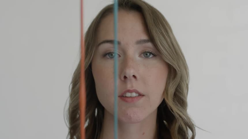 Female painter looks at the camera while the blue and orange paints are being poured in front of her face