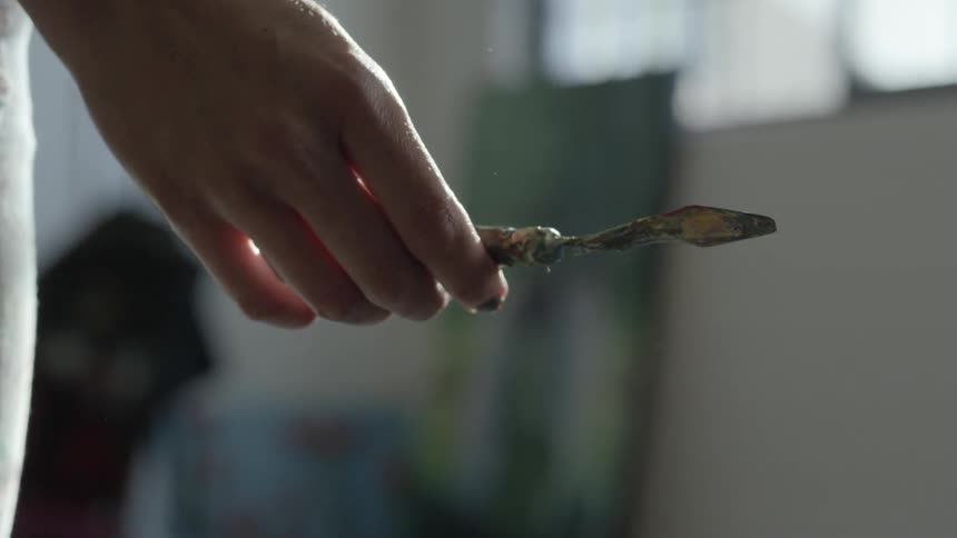 The hand of a woman who is standing indoors can be seen holding a metal paint spreader