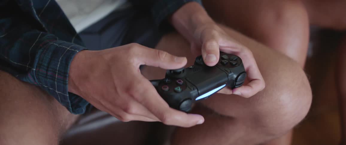 A young male is holding a video game controller in his hands as his pushes buttons and moves the control sticks