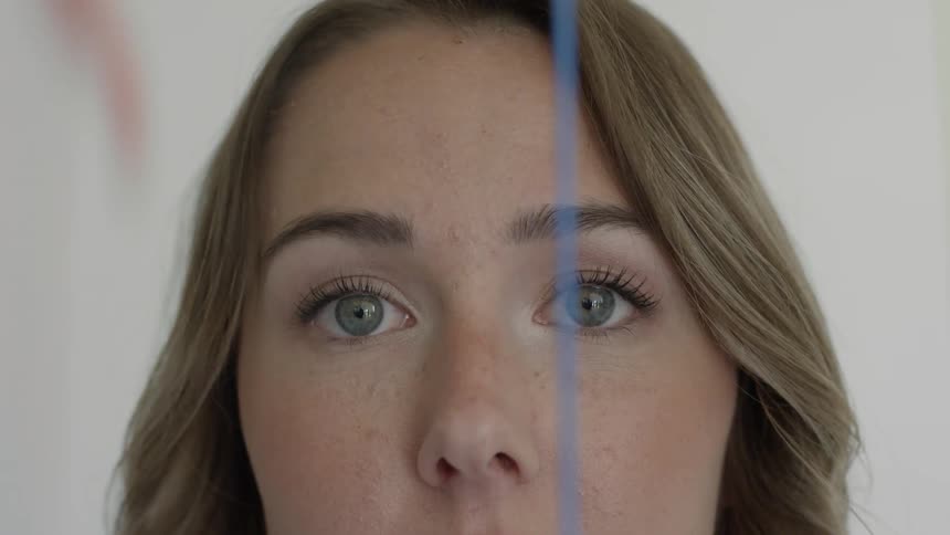 A woman looking into the camera as streams of red blue and yellow paint fall before her face