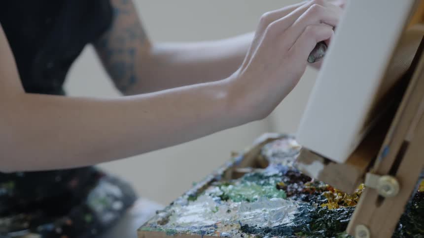 Female artist paints a picture with the brush in a room