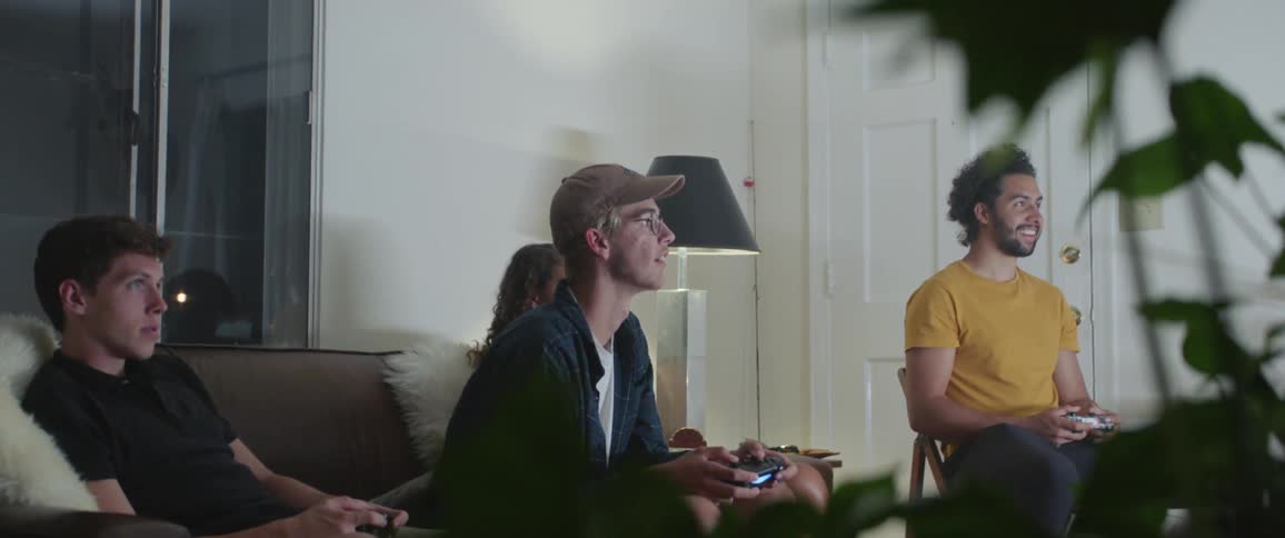 Three males sit and play video games