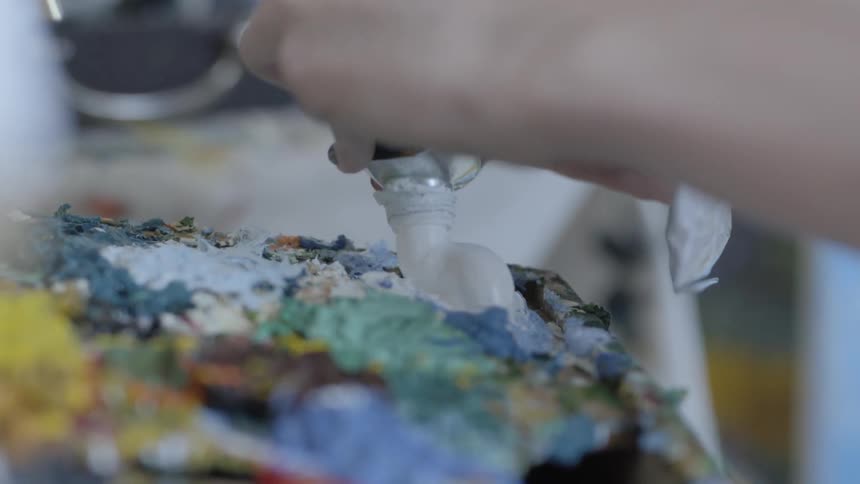 A painter squeezes white paint from a tube onto a palette