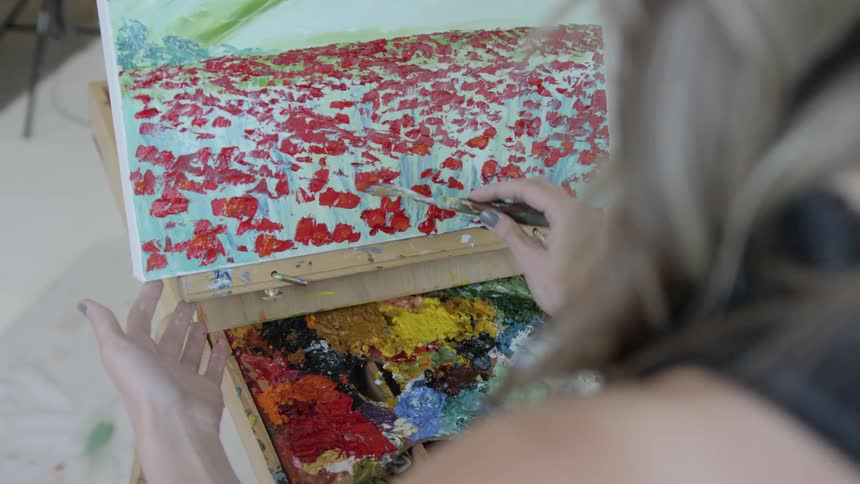 A woman uses a tool to put red paint on a canvas she is painting on