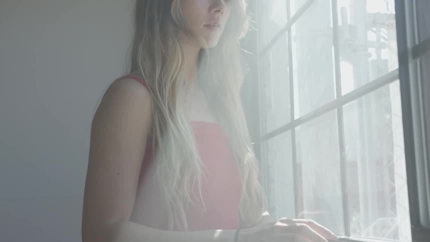 Sad teenage girl standing in the sunlight looking out a window