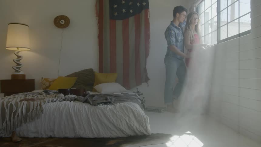 A young man leans up against a young woman as they look out a window