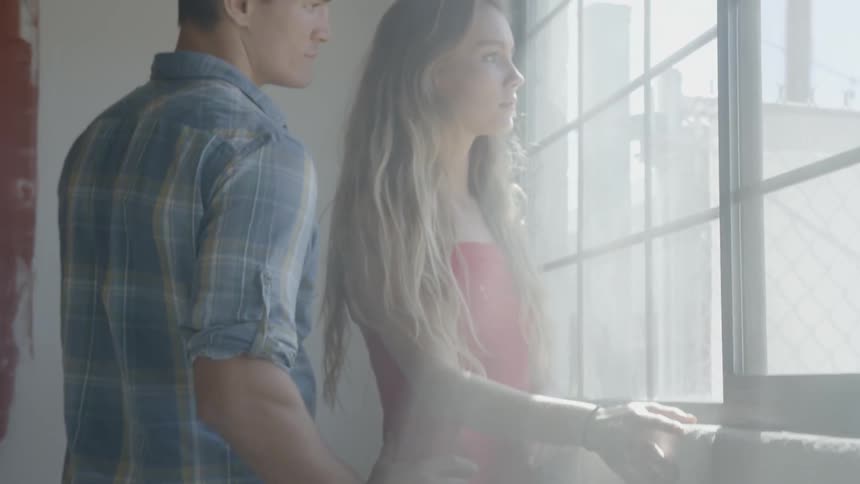 A man walks up to a woman staring out of a window
