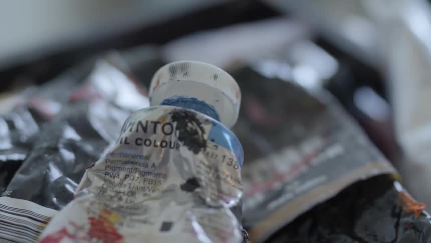 Several tubes of used paint lay in a pile and are covered in splotches of paint