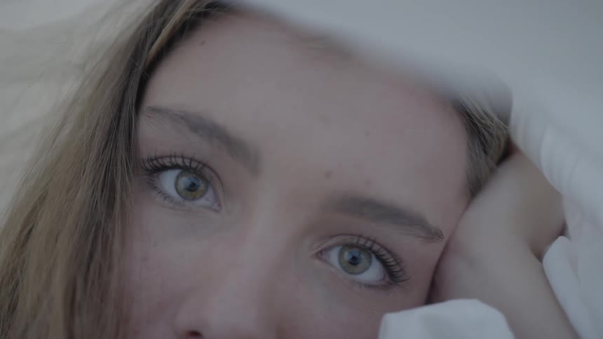 A woman resting her head on her hand under a white cover