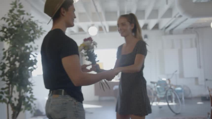 A young male and female playfully dance while the female is holding a bunch of flowers