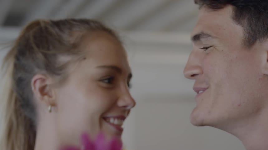 A couple stand and laugh close together with a bouquet of flowers