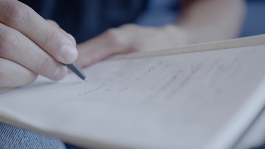 A person writes in a notebook with a pen