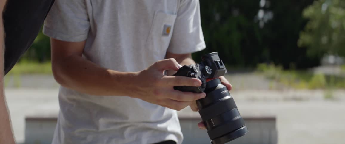 A photographer holds his camera and scrolls through the photos on the display while standing in a skate park