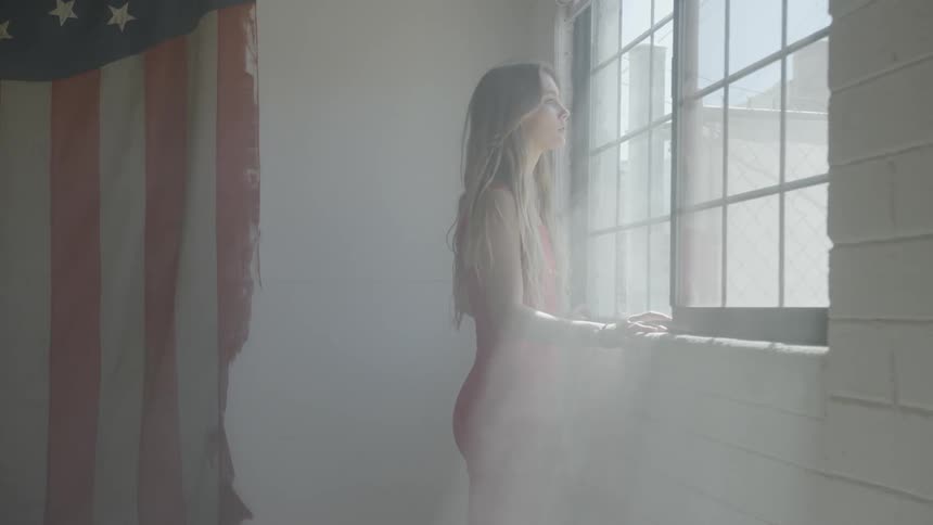 A woman in a red dress stands by a georgian window in a room with an american flag