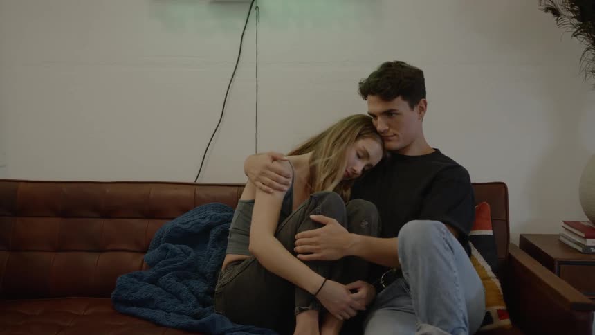A young male and female sitting on a couch lovingly embrace each other