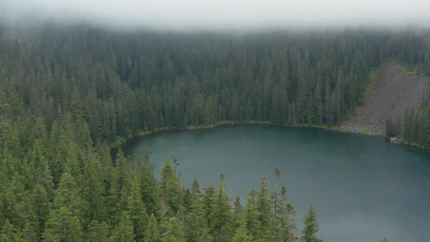 Circular lake is surrounded by forest under a cloudy sky