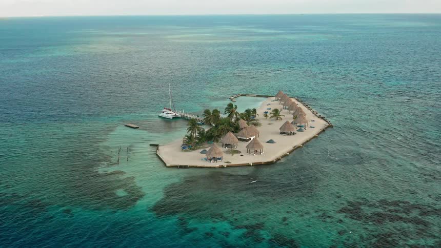 A sailboat is docked at a tiny private tropical island with beach hits and palm trees