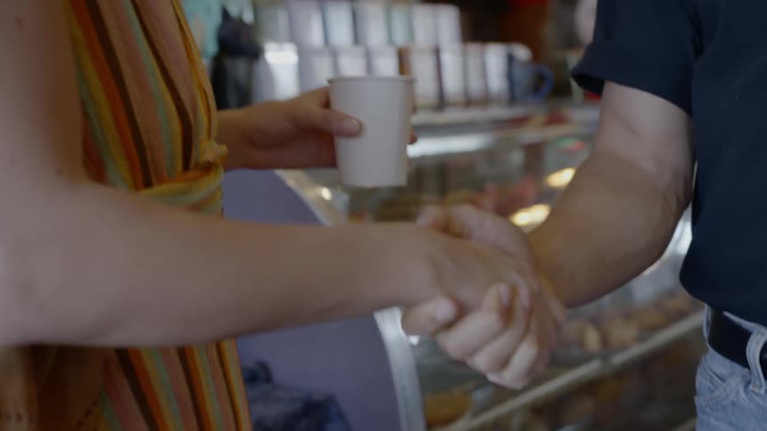 A woman shakes hands iwth a man in the coffee shop