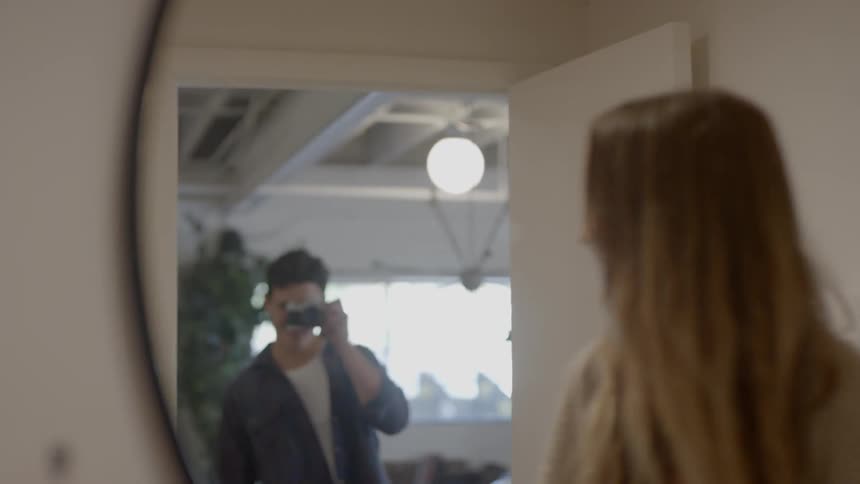 Man takes a picture of the blonde woman who looks in the mirror in the room