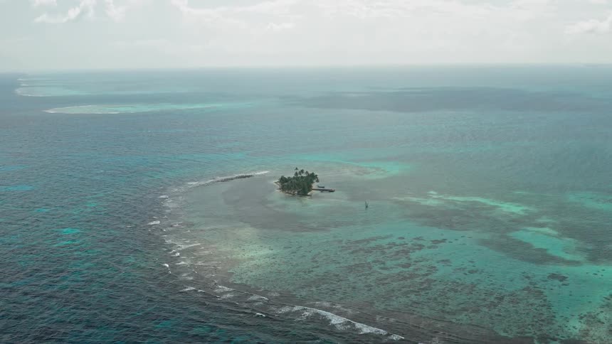 A tiny island with palm trees and a dock in a tropical ocean