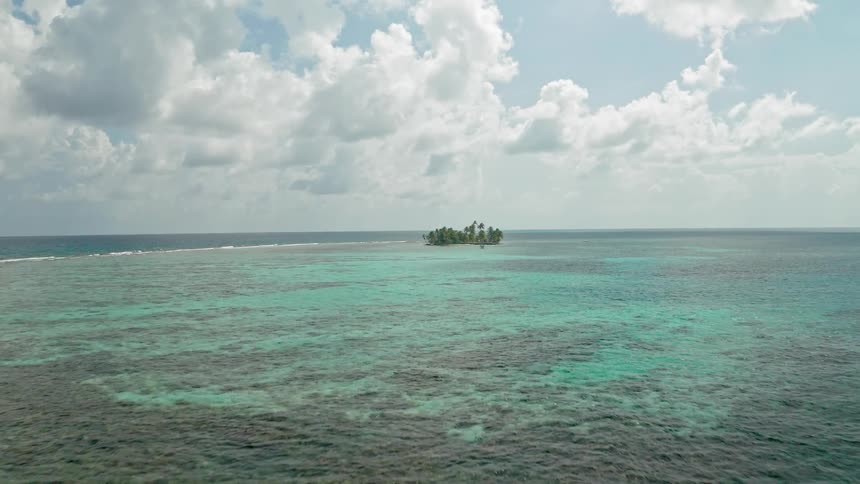 A small island with trees is isolated in the middle of the open ocean