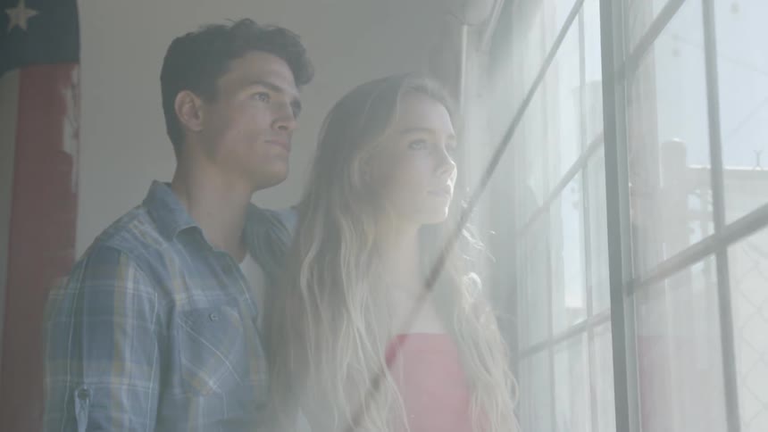 A man and a woman stand beside a window that has beams of light streaming through it