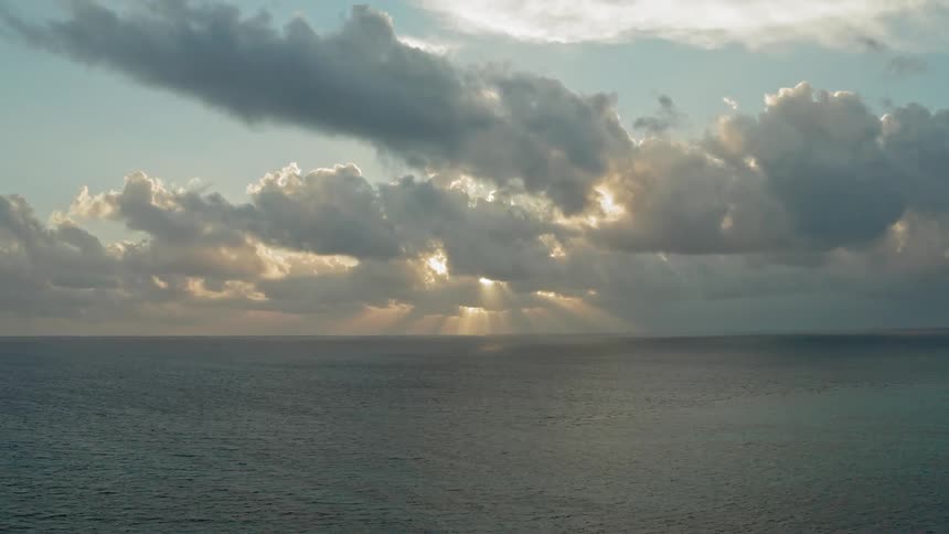 Puffy clouds cover the sun sending rays shining onto the open ocean near dusk