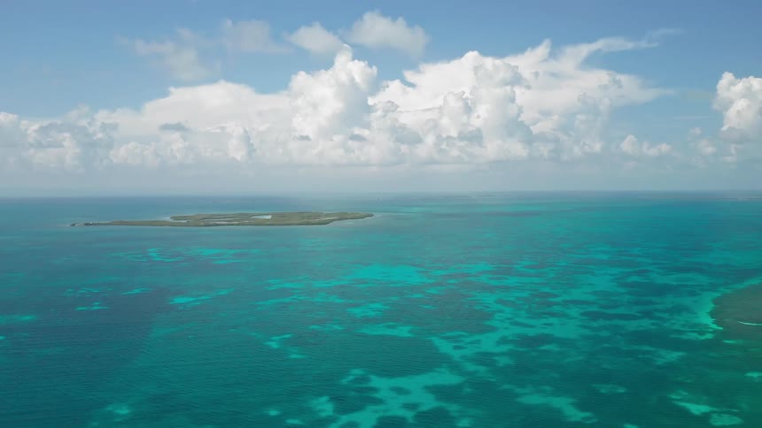 Aerial of a small island in middle of ocean surrounded by clear blue water