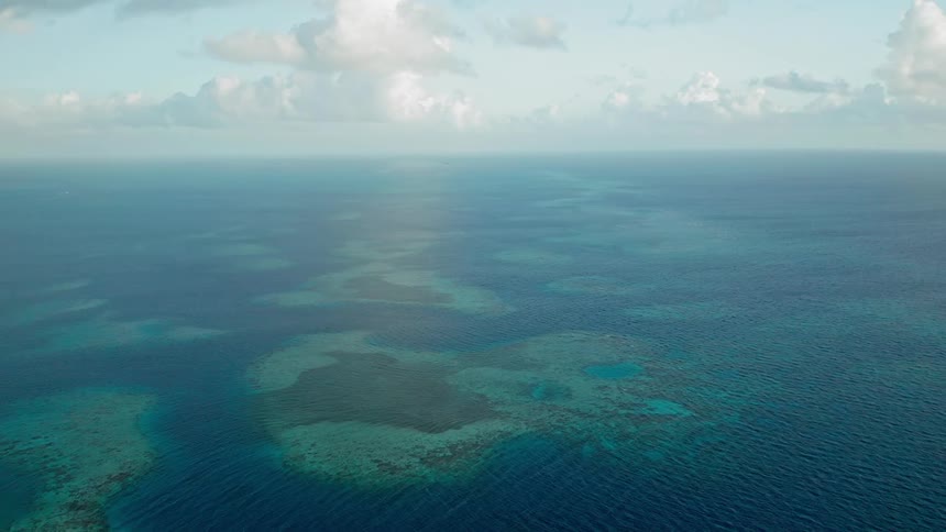 Groups of coral reefs can be seen below the surface of this expanse of ocean