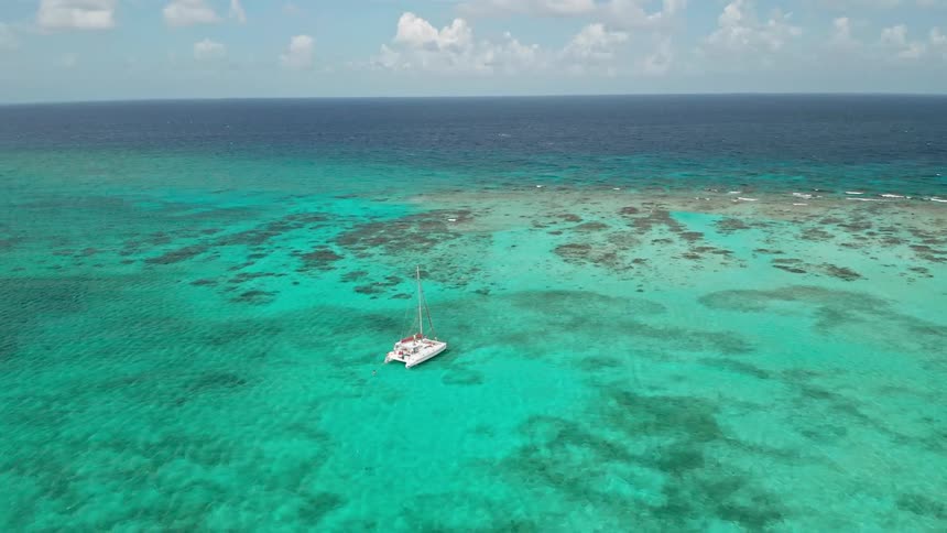 Boat floats over clear bright blue water with darker water on the horizon