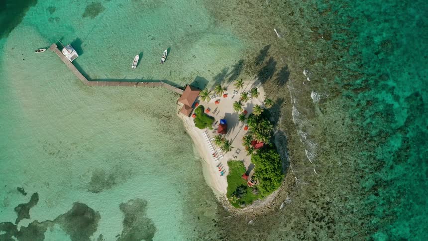 A beautiful island beach resort with a long dock surrounded by clear ocean water on all sides