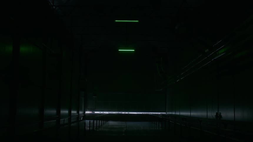 A garage style door slowly closes in a long empty warehouse causing the room to go dark