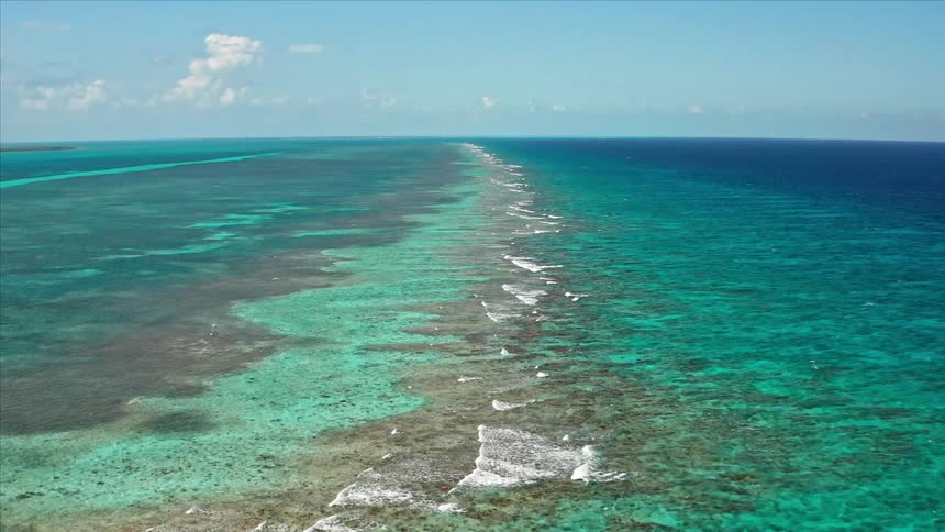 Clear blue water crashes over a reef in a tropical ocean