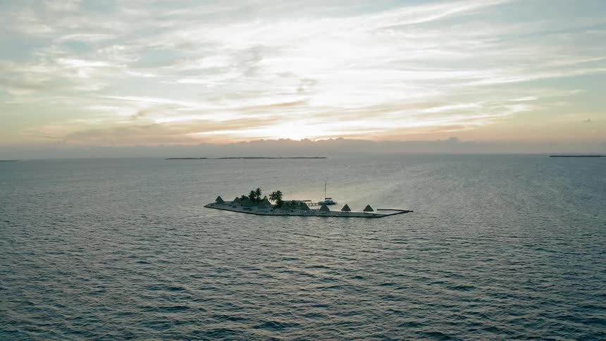 The sun is low in the sky as a very small island stands out from the ocean around it