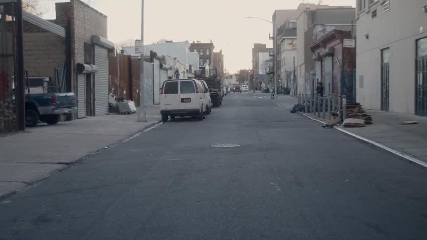 An urban neighborhood with vehicles parked on the side of a narrow road and buildings on each side of the street