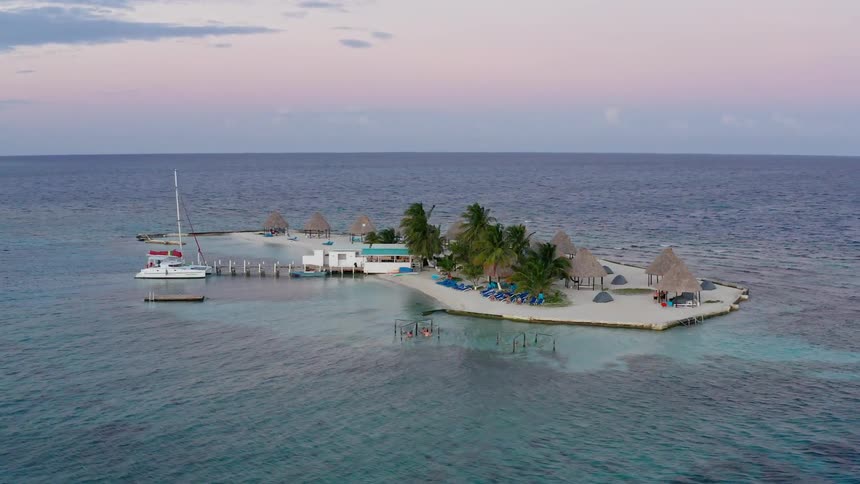A catamaran is docked at a very small sandy island surround by ocean
