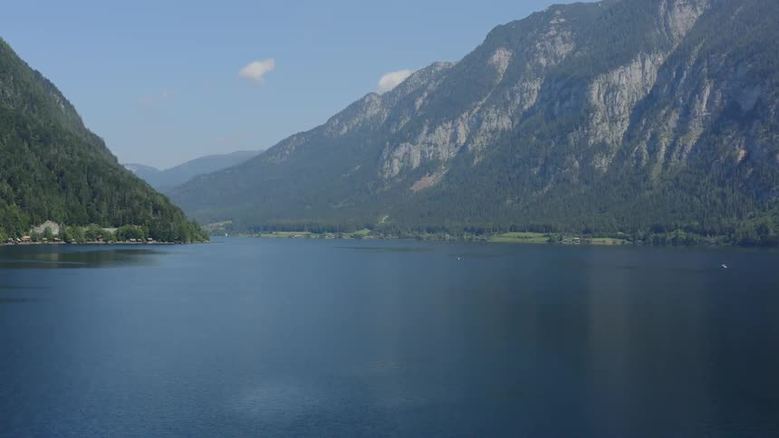 A large body of water is lined by a towering mountain range covered in trees