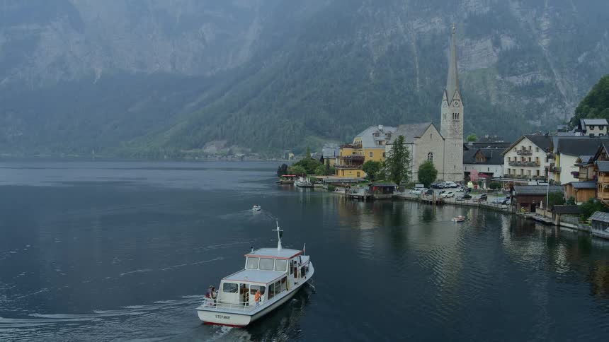A boat sails at the waters edge near a small town with a church nestled by a large mountainside
