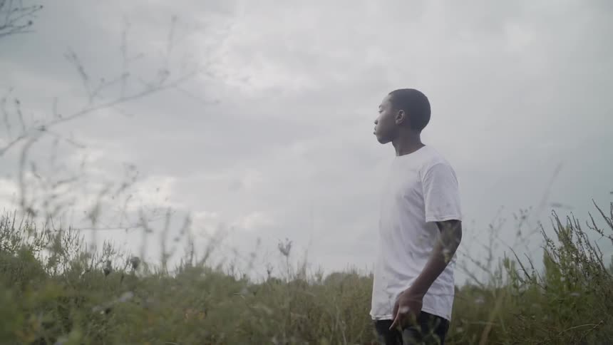 A boy looks around as he walks through tall grass on a cloudy day