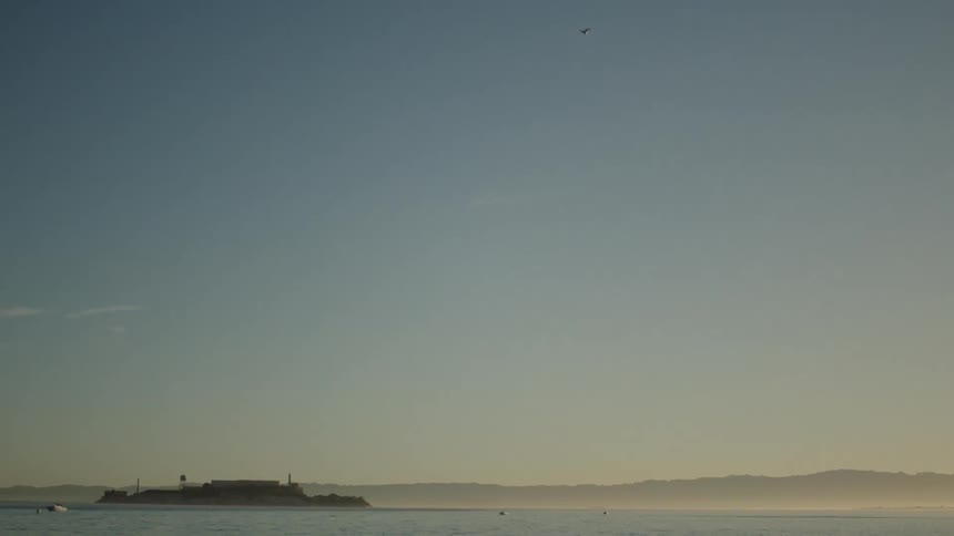 Fog creeps over ocean toward island under clear blue sky