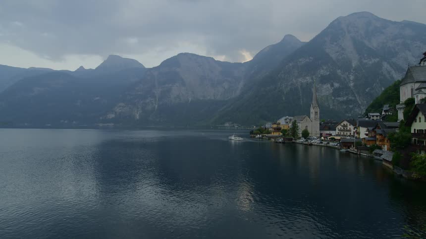 Boat pulls out from dock at town at foot of mountain