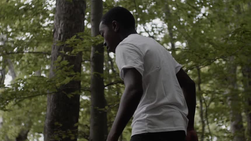 Black teen wears a white shirt as he walks through the woods