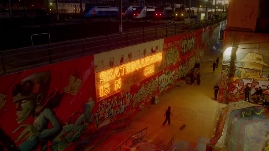 Teens skateboard and hang out in a skateboard decorated with artwork at night