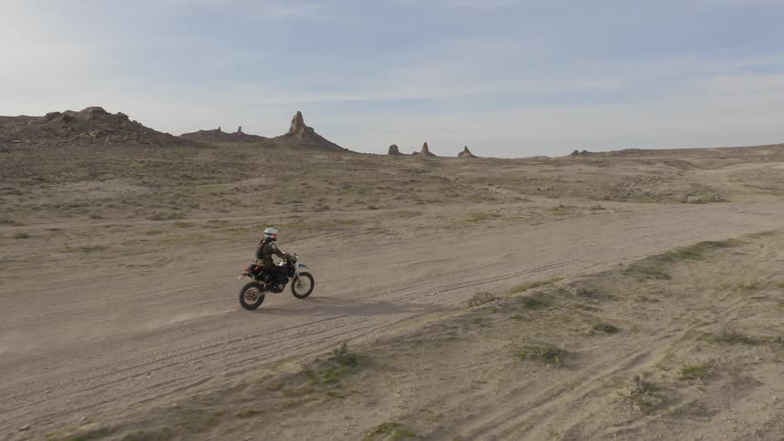 A motorcycle rider stands up while going over a bumpy part of a dirt trail in the desert
