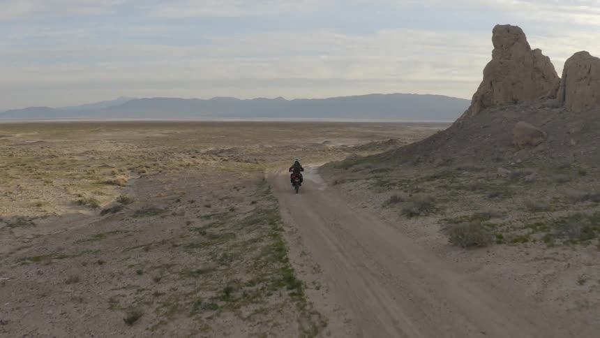 A person rides a motorcycle down a dirt road in a desert like plain