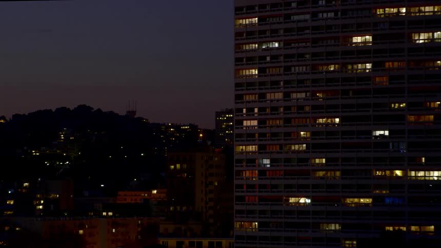 A tall apartment building with lights in various rooms in the middle of a city
