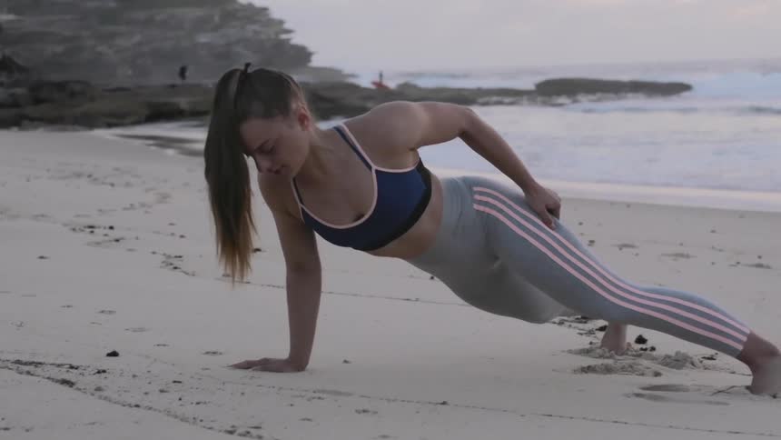 A woman does push ups on a deserted beach