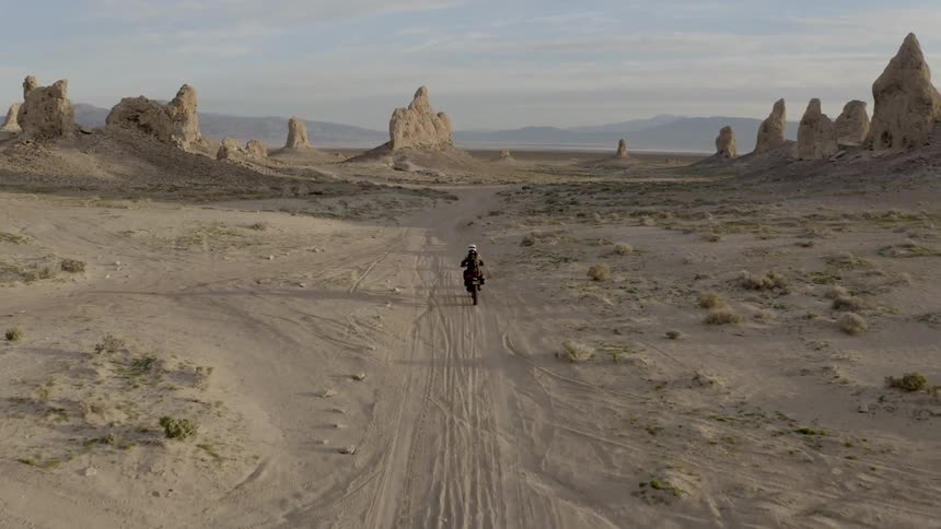 A motorcycle rider drives through the desert and toward rock formations