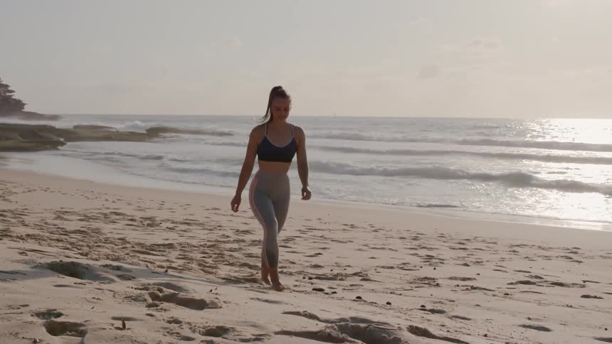 A woman in fitness apparel walks on the beach