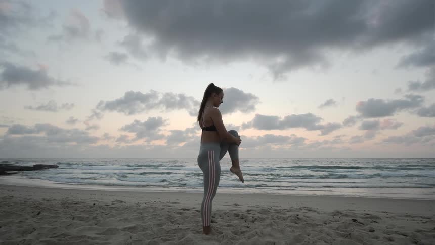 Woman holds yoga position in sand on beach